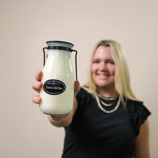 Person holding a 14 oz glass milk bottle with a 'Caramel Cold Brew' label against a plain background