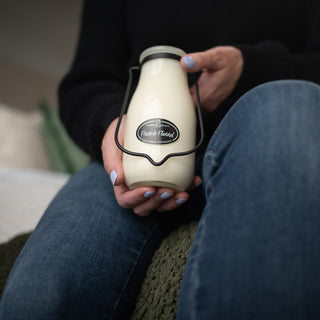 Person holding a 14 oz milk bottle-shaped container with a 'Fireside Flannel' label, sitting on a couch