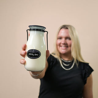 Person holding a 14 oz glass milk bottle with a 'Holiday Home' label against a plain background
