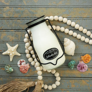 14 oz white milk bottle candle labeled 'Saltwater Mist', surrounded by seashells and beads on a wooden surface