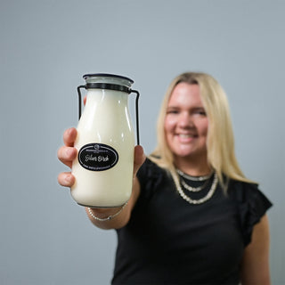 Person holding a glass 14 oz milk bottle with a 'Silver Birch' label against a plain background
