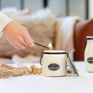 Person lighting a 16 oz candle with a match and 'Eucalyptus Lavender' label, surrounded by decorative items on a table.