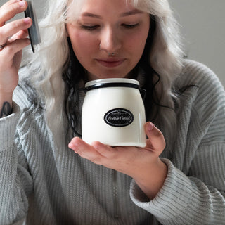Person holding a 16 oz candle in a white container with a 'Fireside Flannel' label, against a neutral background