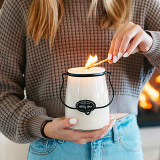 Person lighting a 22 oz candle labeled 'Holiday Home' with a fireplace in the background
