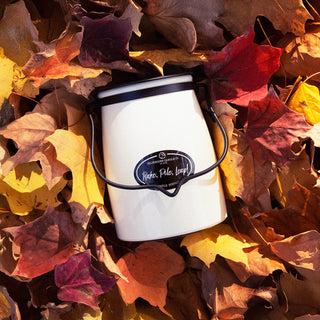 22 oz white candle container with a black lid labeled 'Rake, Pile, Leap!' on a bed of autumn leaves