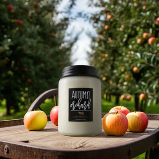 Candle labeled 'Autumn Orchard' on a wooden table with apples in an orchard setting