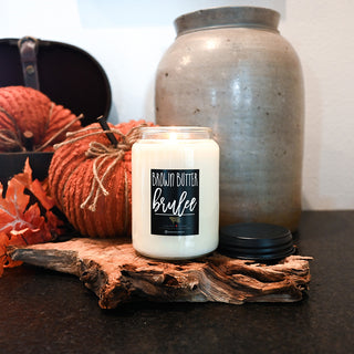 Candle labeled 'Brown Butter Brulee' on a wooden surface with pumpkins and a ceramic jar in the background.