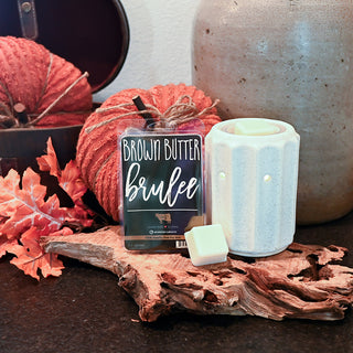 Candle labeled 'Brown Butter Bruèleé' with a lit candle on a wooden surface.