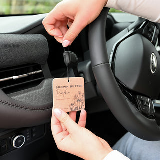 Person hanging a car air freshener labeled 'Brown Butter Pumpkin' in a car's air vent.