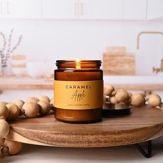 Caramel apple scented candle in an amber jar on a wooden surface with a blurred background