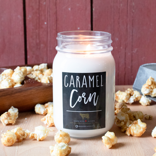 13 oz lit mason jar 'Caramel Corn' candle with caramel corn around on a wooden surface with a red wood background