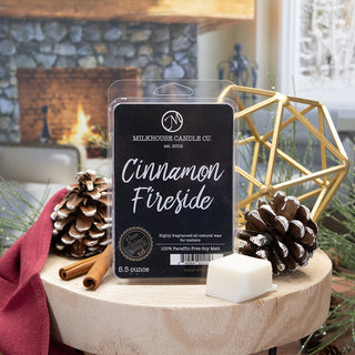 Milkhouse Candle Co. Cinnamon Fireside scented wax melt in a clear pack, displayed on a wooden stand with pinecones, cinnamon sticks, a white wax cube, and a warm fireplace background.
