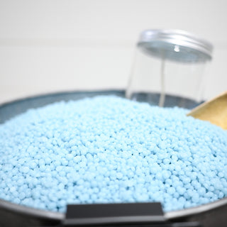 Close-up of blue wax beads in a container with a spoon