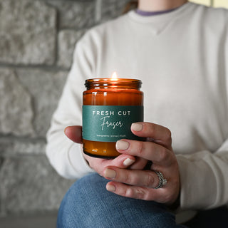 Person holding a 'Fresh Cut Fraser' candle in front of a stone wall