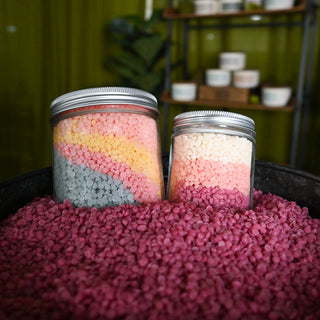 Two jars with colorful contents on a pink textured surface, blurred green background