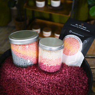 Two jars with colorful contents on a red surface, next to a package of scented wax beads.