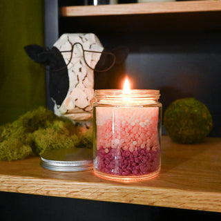 Candle in a glass jar with pink and white beads on a wooden surface