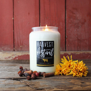 Candle labeled 'Harvest Festival' with yellow flowers and spices on a wooden surface
