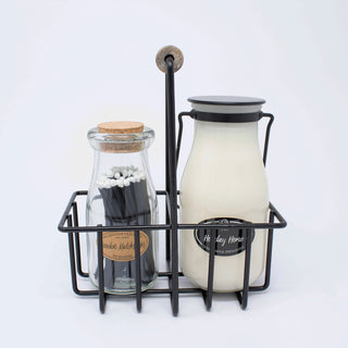 A milk-bottle candle with black metal handle & lid and matchstick bottle in a black metal carrier against a white background