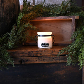 Small white lantern with black handle on a wooden shelf surrounded by greenery