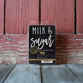 Milk and Sugar wax melt package on a wooden surface with a red wooden background