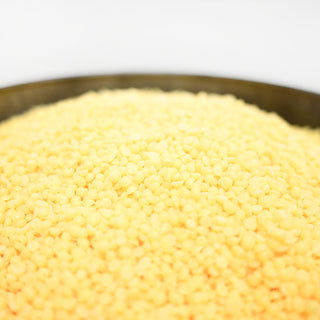 Close-up of yellow scented wax beads in a metal bowl on a white background