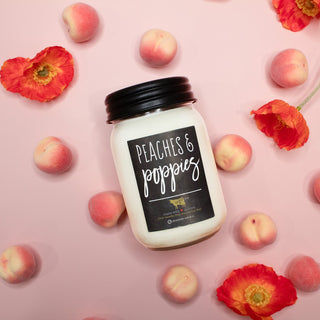 Jar of 'Peaches & Poppies' candle surrounded by peaches and red flowers on a pink background