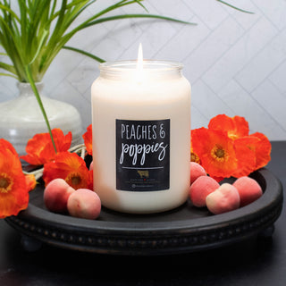 Candle labeled 'Peaches & Poppies' with peaches and flowers on a dark surface
