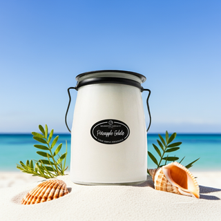 White candle with black lid on a sandy beach with shells and ocean view