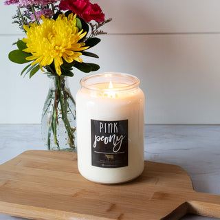 Candle labeled 'Pink Peony' on a wooden board with flowers in the background
