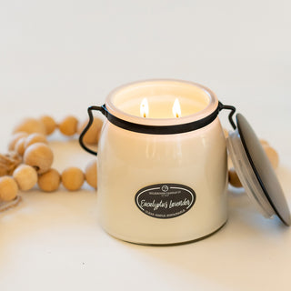 White jarred burning candle, labeled 'Eucalyptus Lavender' on a white surface with decorative wooden beads