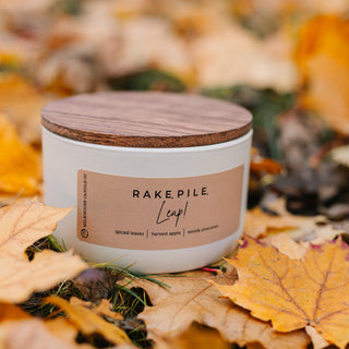 10 oz statement candle with a wooden lid sitting on the ground ontop of autumn leaves
