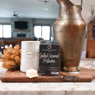 Wax melts labeled 'Salted Caramel Pistachio' with a decorative vase and candle on a wooden board.