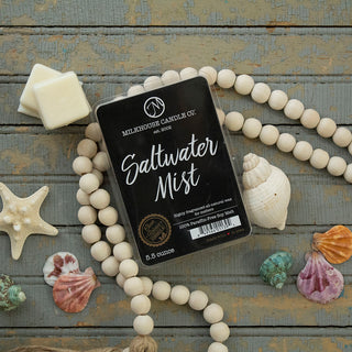 A pack of Milkhouse Candle Co. Saltwater Mist scented wax melts is styled on a rustic gray wooden surface with decorative seashells and white wooden beads.