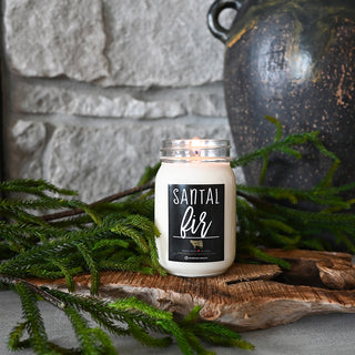 Candle in a jar labeled 'Santal Fir' with greenery and a stone wall in the background