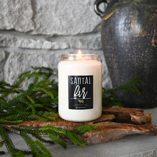 Candle labeled 'Santal Fir' on a stone surface with greenery and a vase.