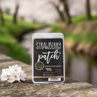 'Strawberry Patch' wax melt package on a stone surface with flowers and blurred natural background
