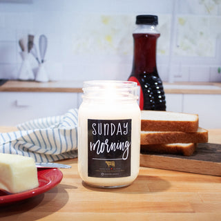 Candle with 'Sunday Morning' label on a kitchen counter with bread and butter