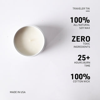 Top-down view of a white soy wax candle in a round white tin on a white background, with black text listing product features: traveler tin, 100% all natural soy wax, zero toxic ingredients, 25+ hours burn time, and 100% cotton wick. Made in USA text appears in the lower left.