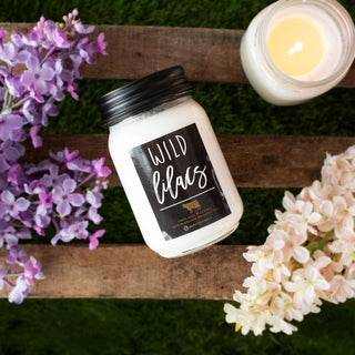 Candle labeled 'Wild Lilacs' with flowers on a wooden surface