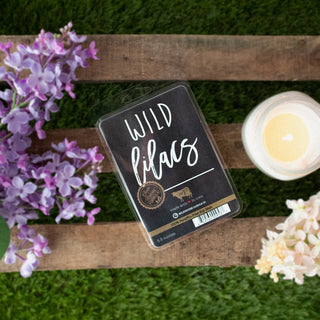 Wax melt package labeled 'Wild Lilacs' on a wooden surface with flowers and a candle
