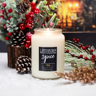 Candle labeled 'Winterberry Spice' surrounded by festive decorations on a white surface