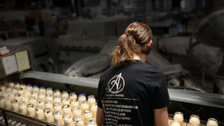 Person wearing a black t-shirt with a logo and text, standing in a production line.
