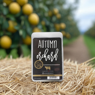 Wax melt package labeled 'Autumn Orchard' on a hay bale with a blurred background of fruit trees