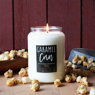 Candle labeled 'Caramel Corn' with popcorn around on a wooden surface