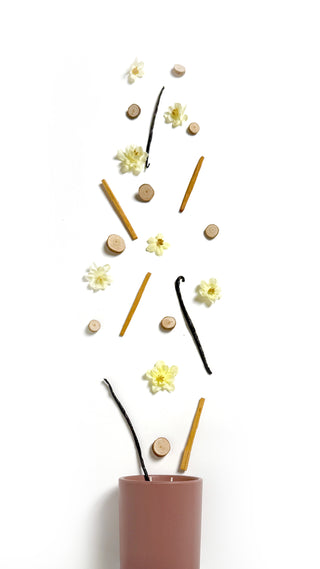Tonka beans, wood bits, white flowers and sandalwood pouring out of a blush colored ceramic jar