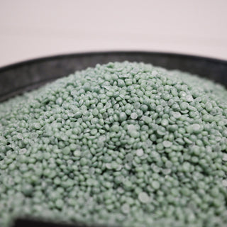 Close-up of green wax beads in a metal container