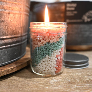 Candle in a glass jar with colorful beads inside, lit on a wooden surface.