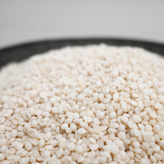 Close-up of white wax beads in a metal container with a white background