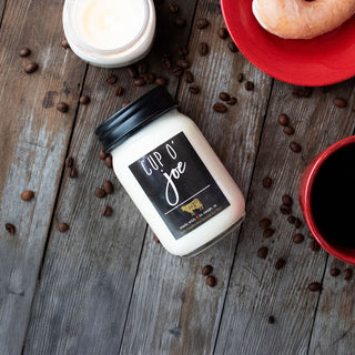 Candle with 'Cup O' Joe' label on a wooden surface with coffee beans and a cup of coffee